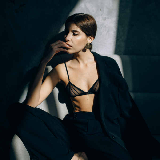 Woman wearing a black bra and pants sitting on a chair with a dark background