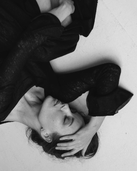 Black and white photo of a person lying on a white surface with their head in their hands.